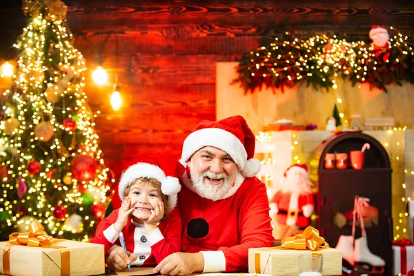 Papai Noel ajudante de Natal e Papai Noel escrevendo ou lendo carta para casa perto da árvore de Natal. Lista de Desejos para Santa . — Fotografia de Stock
