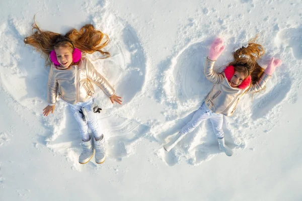 Snow angels made by a kids in the snow. Smiling children lying on snow with copy space. Funny kids making snow angel. Top view. — Stockfoto