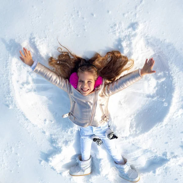 Funny kid making snow angel. Child girl playing and making a snow angel in the snow. Top view. — Stockfoto