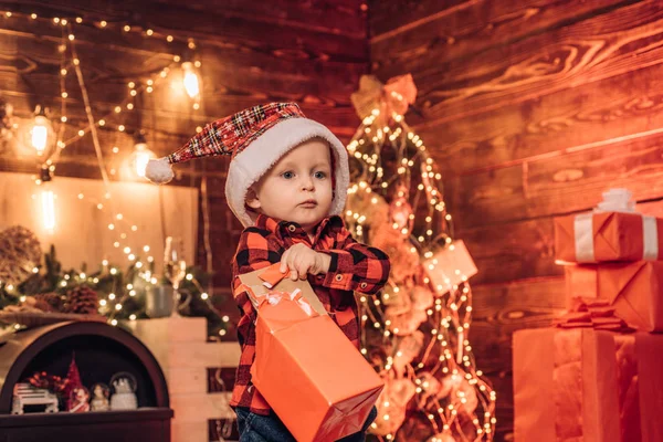 Симпатичный голубоглазый мальчик Санта открывает свой новогодний подарок. Красивый зимний фон. Праздничные скидки Радость и счастье. С Рождеством и Новым годом! . — стоковое фото