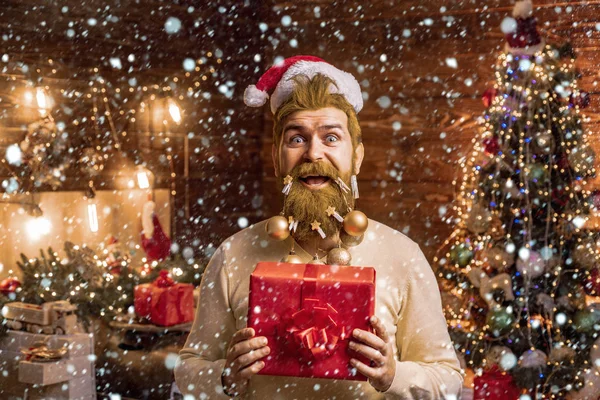 Mann im Schnee. Modeporträt eines gutaussehenden Mannes im Haus mit Weihnachtsbaum. Styling-Weihnachtsmann mit langem Bart posiert auf dem weihnachtlichen Holzgrund. — Stockfoto