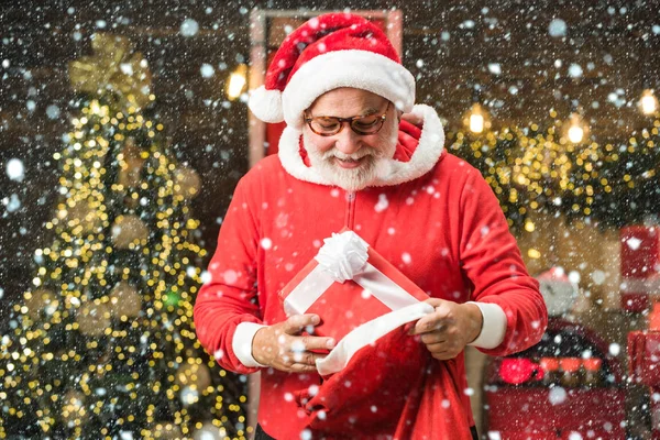 Man in snow. Portrait of handsome Santa man indoors with Christmas gift. Santa old man posing on vintage wooden background.