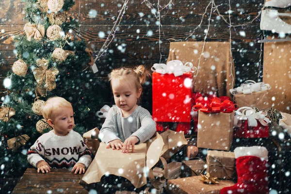 Neujahrskinder. kiddy. Kind mit Weihnachtsgeschenk auf hölzernem Hintergrund. Winterkinder. Eröffnungsgeschenke zu Weihnachten und Neujahr. Lächelndes Kind, das hinter dem Weihnachtsbaum im Wohnzimmer hervorlugt. Kind — Stockfoto