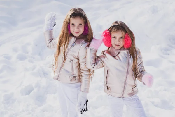 Children in Winter Park playing snowballs. Cute sisters playing in a snow. Winter clothing for baby and toddler. Little girls throw snowball in park. — Stock Photo, Image