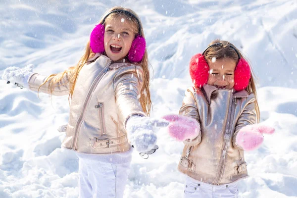 Little girls throw snowball in park. Two adorable young girls having fun together in beautiful winter park. Winter child. Winter clothing for baby and toddler. — Stock Photo, Image