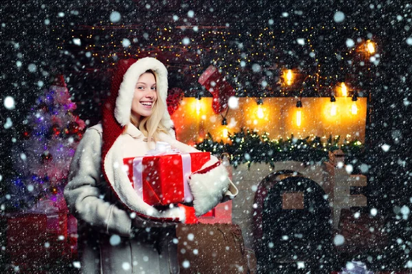 Christmas and new year concept. Girl in snow. Woman in red Santa hat holding present. Blonde Santa woman holding gift box at vintage wall. Christmas fashion. — Stock Photo, Image