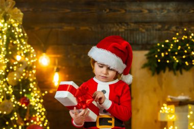 Mutlu çocuk iki eliyle kırmızı bir hediye kutusu tutuyor. Noel Baba 'nın portresi kameraya bakıyor. Küçük şirin çocuklar Noel 'i kutluyor..