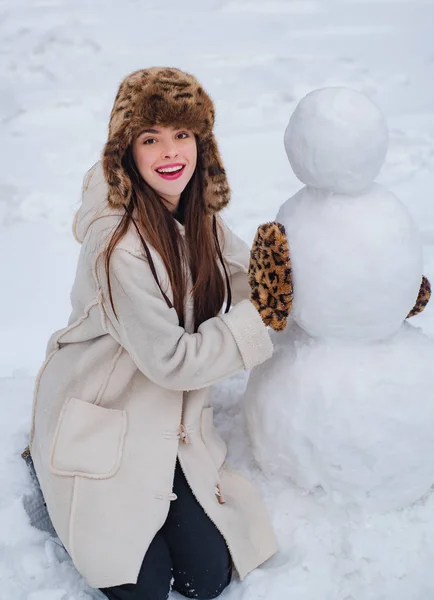 冬の天候にポーズ面白いサンタの女の子。冬の公園で雪だるまと遊ぶ女の子。メリークリスマスとハッピーホリデー。女の子のための雪だるまと冬の楽しみを作る. — ストック写真