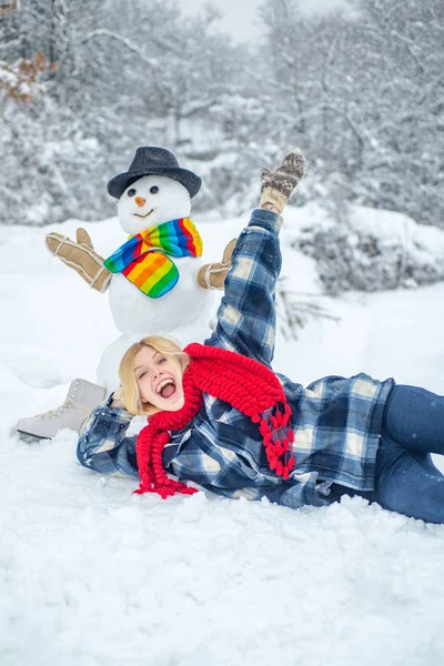 Greeting snowman. Snowman and funny female model standing in winter hat and scarf with red nose. Cute snowman at a snowy village. — Stock Photo, Image