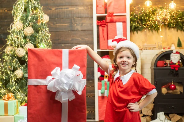 Menina feliz segurando uma grande caixa de presente vermelho. Miúdo a divertir-se perto da árvore de Natal dentro de casa. Serviço de entrega de inverno para crianças . — Fotografia de Stock