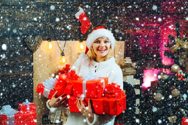 Rapariga na neve. Jovem com caixas de presente de Natal na frente da árvore de Natal. Jovem alegre vestindo traje de Natal sobre a parede de madeira. Retrato de uma jovem mulher sorridente . — Fotografia de Stock