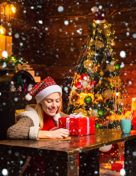 Woman is writing a christmas letter. New Year mood. Attractive woman in a Christmas room. Happy woman with Christmas gift over Christmas interior background. Girl in snow.