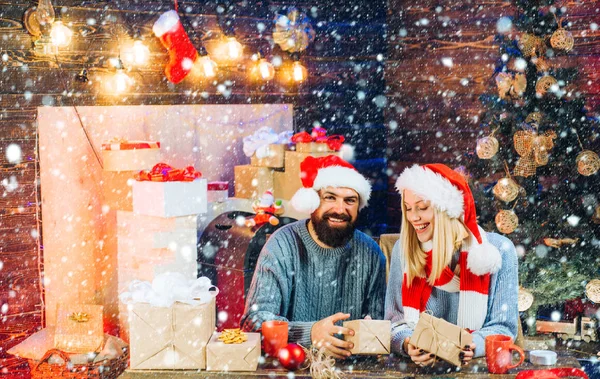 Ett par i snö. Söt ung kvinna och stilig man med tomteluva. Kärlek. Nyårsfamilj med julklappslådor framför julgranen. Julpar. Julgran dekorera hemma. — Stockfoto