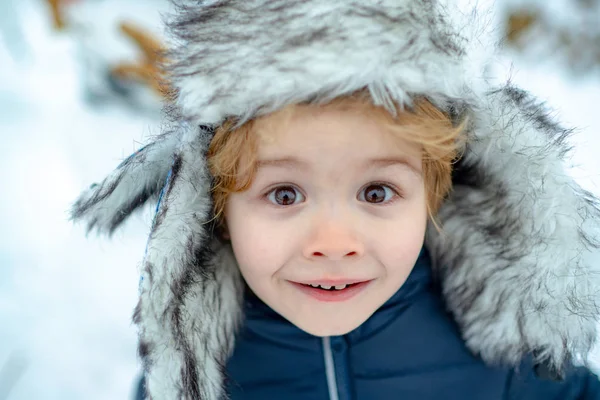 Winter kid excited face close up. Happy winter time. Happy child playing with snow on a snowy winter walk.