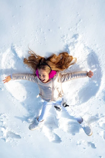 Leende barn liggande på snö med kopieringsutrymme. En lustig grabb som gör snöängel. Barn flicka leka och göra en snö ängel i snön. — Stockfoto