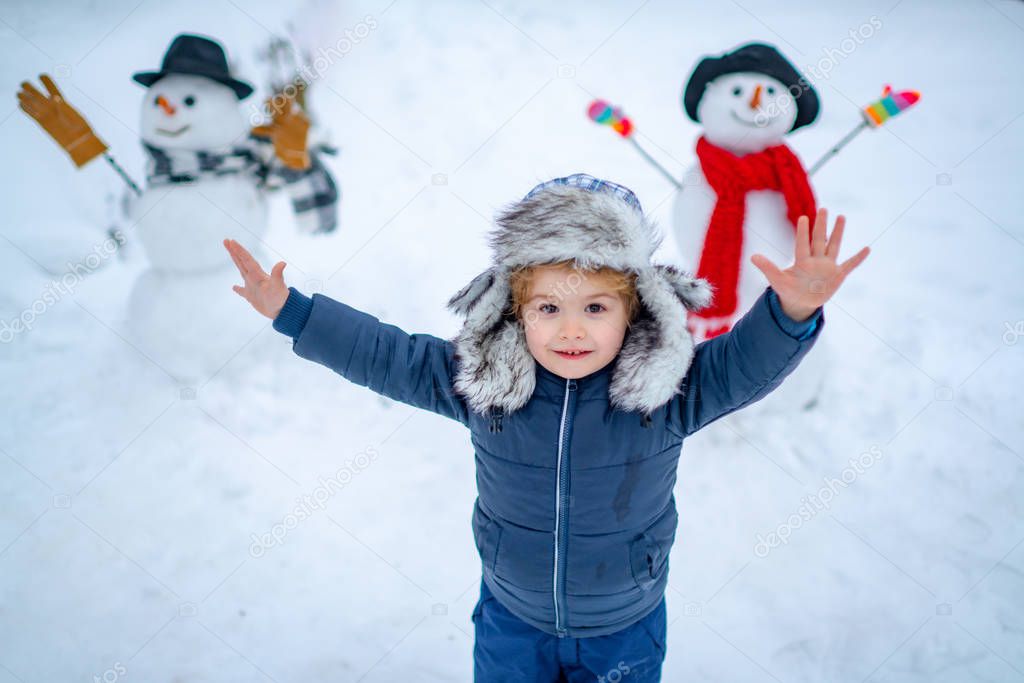 Beauty Winter child with snowman in frosty winter Park. Outdoor portrait of little son in cold sunny winter weather in park. Winter emotion.