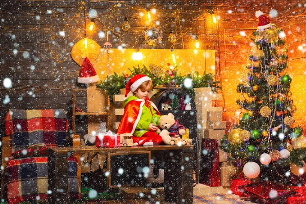 Niño sentado en una mesa de madera y jugando con regalos. Niña en la nieve. Juguetes cerrados y abiertos. Juguetes naturales de madera y textiles para niños juegan. Árbol de Navidad y año nuevo —  Fotos de Stock