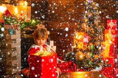 Büyüleyici bebek Noel Baba kışın Noel arkaplanda çelenk ışıklarıyla sihirli hediye kutusuna bakıyor. Tatiller ve kış çocukluğu kavramı. Güzel bebek, Noel 'in tadını çıkar. Kardaki çocuk.