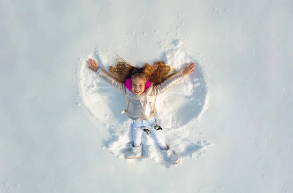 Snow angel made by a kid in the snow. Smiling child lying on snow with copy space. Funny kid making snow angel.