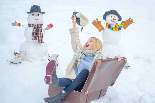Egy lány bőrönddel. Winter World Travel - Szánkó bőrönd. Téli vakációkat tervezek. Téli szünet. Boldog mosolygós hóember és téli lány a napsütéses napon. — Stock Fotó