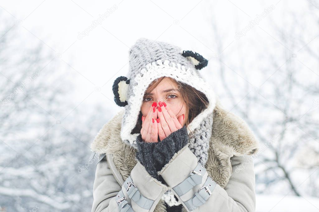 Young woman with nose wiper near winter tree. Woman with napkin sneezing in the winter snowy park. Young woman having flu and blowing her nose.
