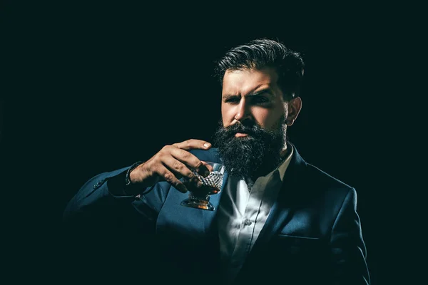 Bärte und ein Glas Whiskey. Barkeeper mit Bart hält Glasschnaps in der Hand. Alkohol-Konzept. Eleganter, bärtiger Mann Barkeeper hält Whiskey-Glas. — Stockfoto