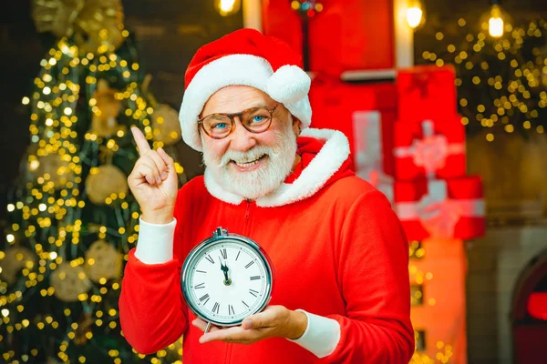 サンタクロースは、クリスマスや新年のカウントダウンと時計を保持木製の家のインテリアにサンタクロースは、時計の時間を示しています。ハッピークリスマスサンタ. — ストック写真