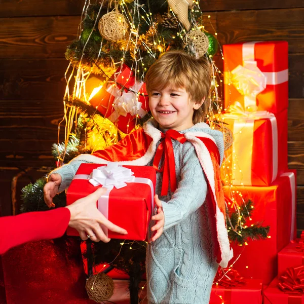 Junge bekommt Geschenk von seiner Mutter. glückliches Kind, das mit beiden Händen eine rote Geschenkschachtel hält. Neujahrskinder. Frohe Weihnachten und frohe Feiertage. lustiges Kind mit Weihnachtsgeschenk. — Stockfoto