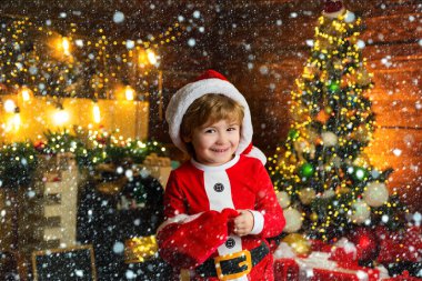 İnternetten noel hediyesi al. Noel alışverişi konsepti. Tatiller ve kış çocukluğu kavramı. Noel Baba şapkalı gülümseyen küçük çocuk arka plandaki Noel ağacında.