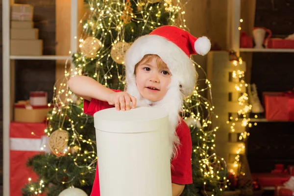 Kleine Weihnachtsmann-Helferin mit Weihnachtsgeschenk. fröhliches süßes Kind öffnet ein Weihnachtsgeschenk. — Stockfoto