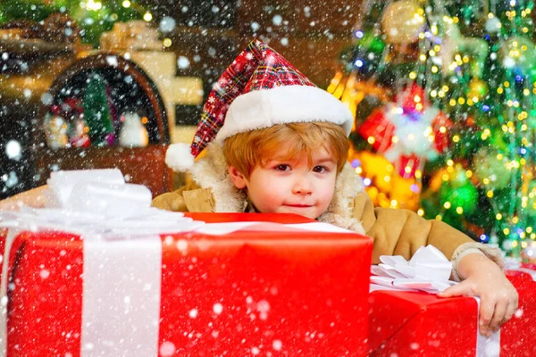 Ευτυχισμένο χαριτωμένο παιδί σε Σάντα καπέλο με δώρο έχουν τα Χριστούγεννα. Αστείο παιδί που κρατάει Χριστουγεννιάτικο δώρο. Χριστουγεννιάτικη γιορτή. — Φωτογραφία Αρχείου