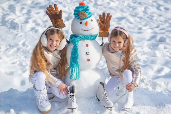 Rendre le bonhomme de neige et l'hiver amusant pour les enfants. Enfants heureux jouant avec un bonhomme de neige lors d'une promenade hivernale enneigée. — Photo