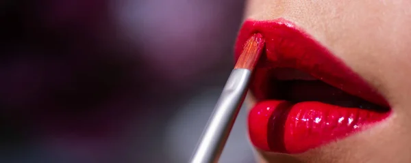 Closeup sexy lips with lipstick. Beautiful young woman painting red lipstick on lips. Young woman applying her makeup. Dyes her lips lipstick red color. — Stock Photo, Image