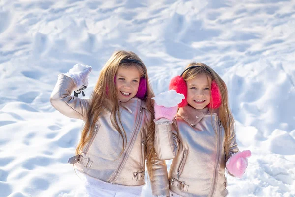 Les petites filles jettent des boules de neige dans le parc. Portrait de deux petites filles jouant avec la neige en hiver. Jolies soeurs jouant dans la neige. Enfants d'hiver posant et s'amusant. Portrait de femme enfant. — Photo