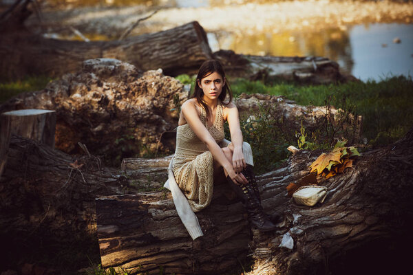 Portrait of a beautiful woman in a light dress. Young beautiful girl. Copy space. Place for text. Art work of romantic woman. Portrait of serious woman on trunk wood. Sunny day