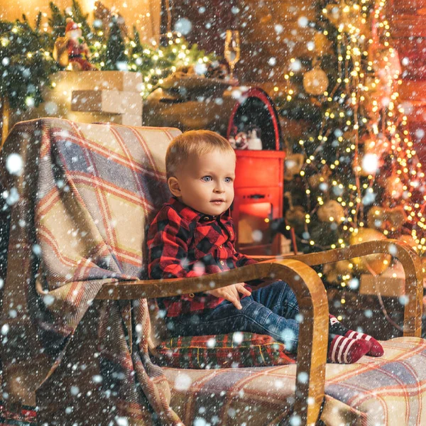 Kleines Baby, das im Stuhl auf dem weihnachtlichen Hintergrund sitzt. Frohe Weihnachten und frohe Feiertage. — Stockfoto