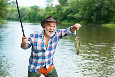 Balık yakalayan sakallı adam. Erkek hobisi. Suyun arka planında ormanın bir yansıması var. Emeklilik sadece bir başlangıç. İyi balık avları. Sadece bunu yap..