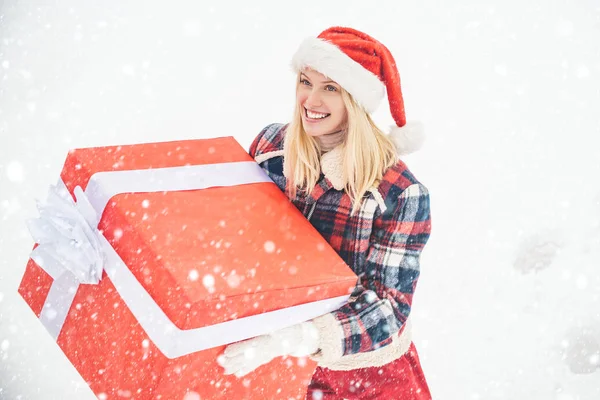 Santa femme tient une grande boîte cadeau avec de l'espace de copie pour votre texte. Fille de Noël tenant un grand cadeau. Grande boîte cadeau. Fille de Noël fou pousse un gros cadeau sur fond d'hiver de neige. — Photo