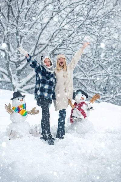Két mosolygó barát hóembert csinál karácsonykor. Hogy a hóember és a tél szórakoztató a lány. Vicces Mikulás lány pózol a téli időjárás. — Stock Fotó