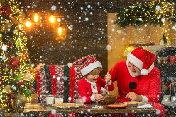 Kid Papai Noel desfrutando em bolo de gengibre servido e leite. Pai Natal e filho se divertindo perto da árvore de Natal e celebrar o Natal em casa. Miúdo engraçado fazer biscoitos de Natal. — Fotografia de Stock