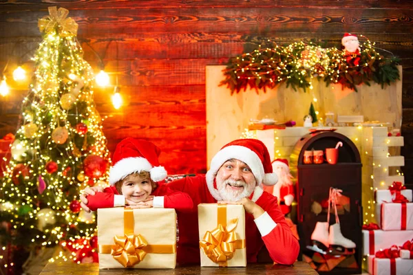 Menino Papai Noel com um presente cheio de presentes. Para cartazes de Natal e Ano Novo. Adorável criança filho e avô jogar Santa em casa . — Fotografia de Stock