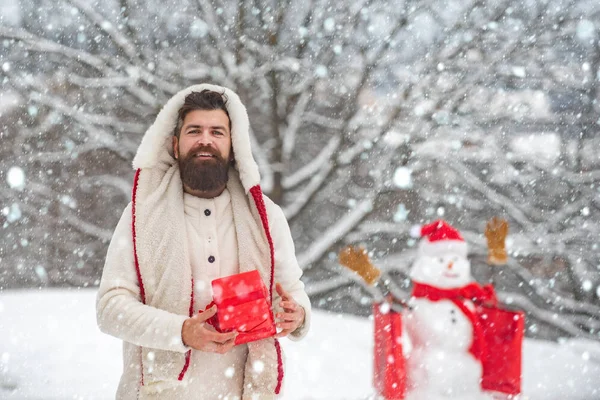 Happy smiling snow man on sunny winter day with Happy father. Cute little snowman and bearded man with shopping bag. Hipster santa claus. Delivery gifts.