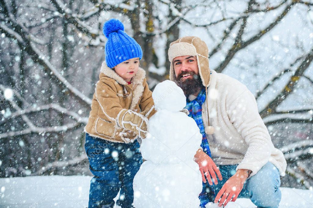 Father and son making snowman. Dad and baby son playing together outdoors. Happy father and son - winter portrait.