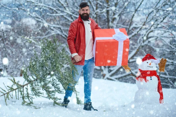 Mann im Weihnachtskleid mit Geschenk in der Nähe des weihnachtlichen Hintergrunds. glücklicher Vater mit Weihnachtsgeschenk über Winter Schneemann Hintergrund. — Stockfoto