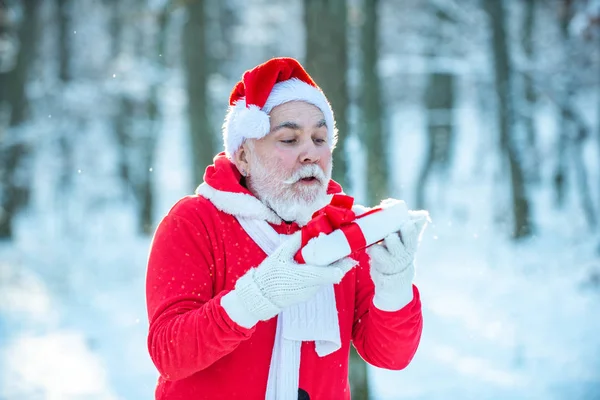 Дедушка Санта гуляет по лесу. Настоящий Санта-Клаус в красной кепке тянет большой красный мешок с подарками. Санта с мешком подарков против снежной сцены . — стоковое фото