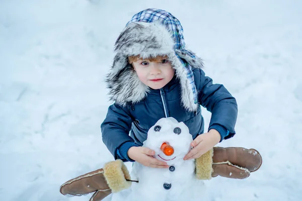Kar Bahçesindeki sevimli çocuğun kış portresi. Noel kış çocukları. Kardan arka planda Kardan Adam ile oynayan çocuk. — Stok fotoğraf