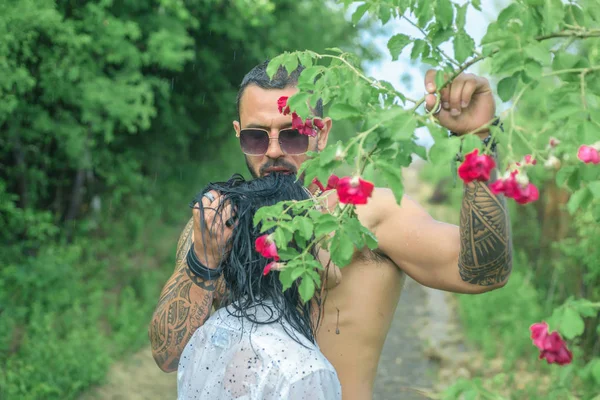 Mulher sexy e apto e abraçando homem bonito com tatuagem. Amor e confiança. Homem sem camisa e bela mulher magra apaixonadamente beijar. Natureza . — Fotografia de Stock