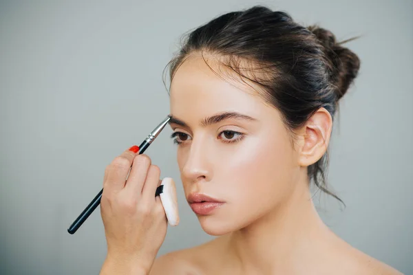 Schöne junge Frau bekommt Augenbrauen-Make-up. trägt die Künstlerin mit einem Pinsel Lidschatten auf ihre Augenbraue auf. junges Model-Mädchen bekommt ihr natürliches Augenbrauen-Make-up. — Stockfoto