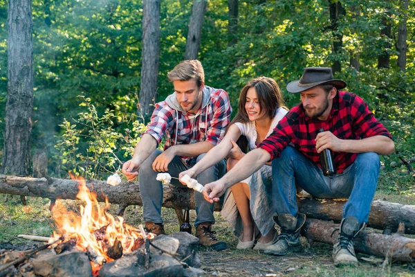 Les amis apprécient barbecue week-end en forêt. Amis de la compagnie pique-nique ou barbecue rôtissant des guimauves près du feu de joie. Groupe de randonneurs se relaxant près du feu de camp. Grillage des guimauves barbecue . — Photo