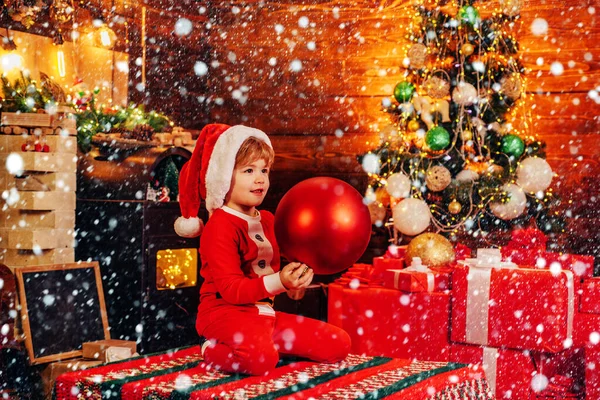 小さなサンタクロースはクリスマスツリーのための巨大な装飾的なボールで自分自身を助けます。クリスマスの属性。メリーと明るいクリスマス。クリスマスの魔法の贈り物とサンタのヘルパー. — ストック写真